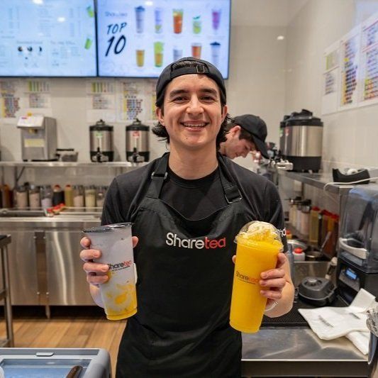 Smiling staff member in a smoothie shop holding two colorful drinks behind the counter