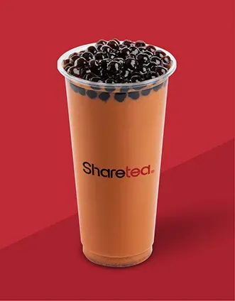 Tall orange bubble tea with black tapioca pearls in a clear cup on a red background