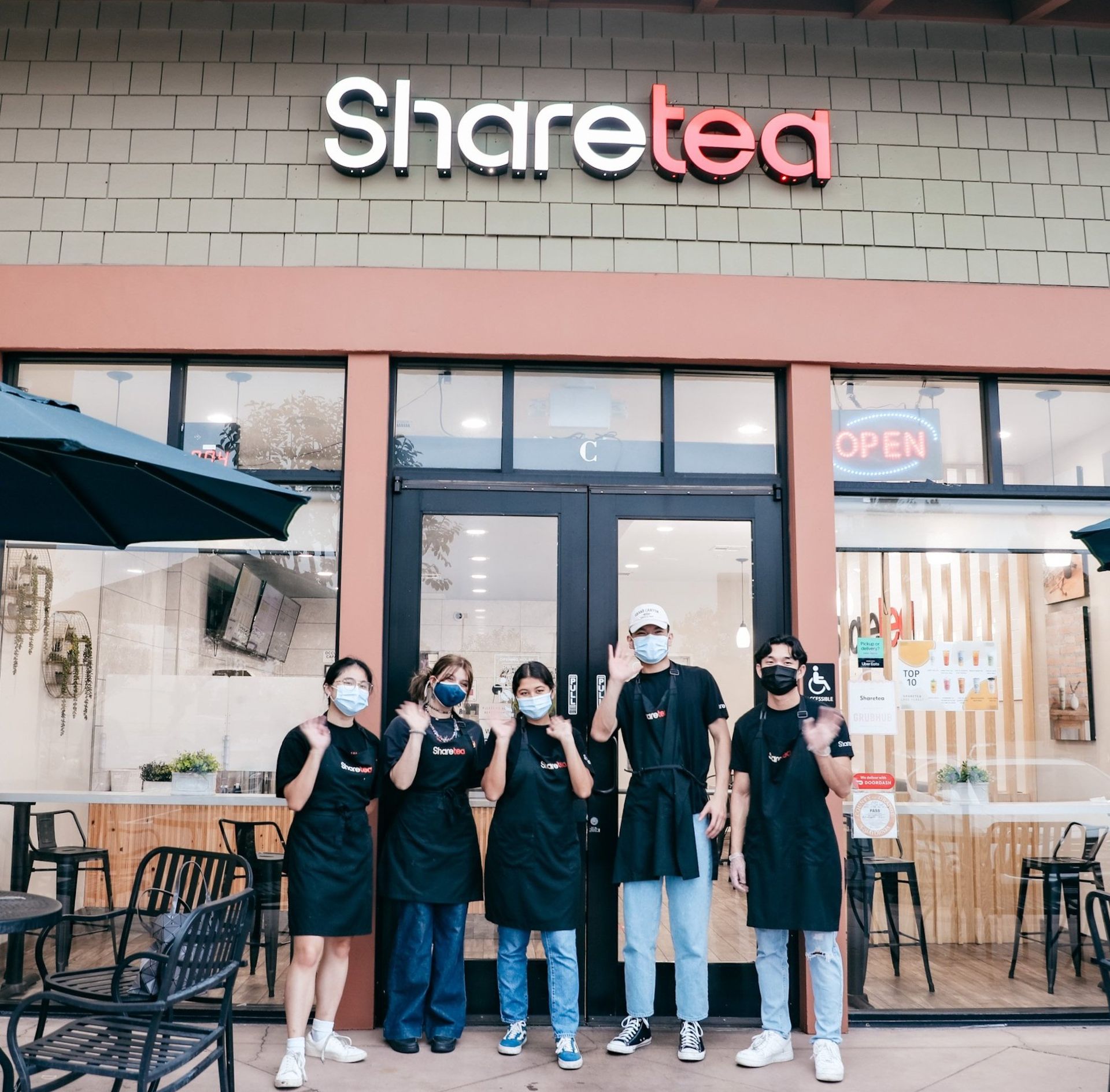 Five masked people pose outside a Sharetea storefront with an open sign.