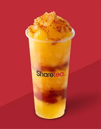Tall fruit drink in a clear cup, orange and yellow with red syrup, topped with shaved ice on a red background