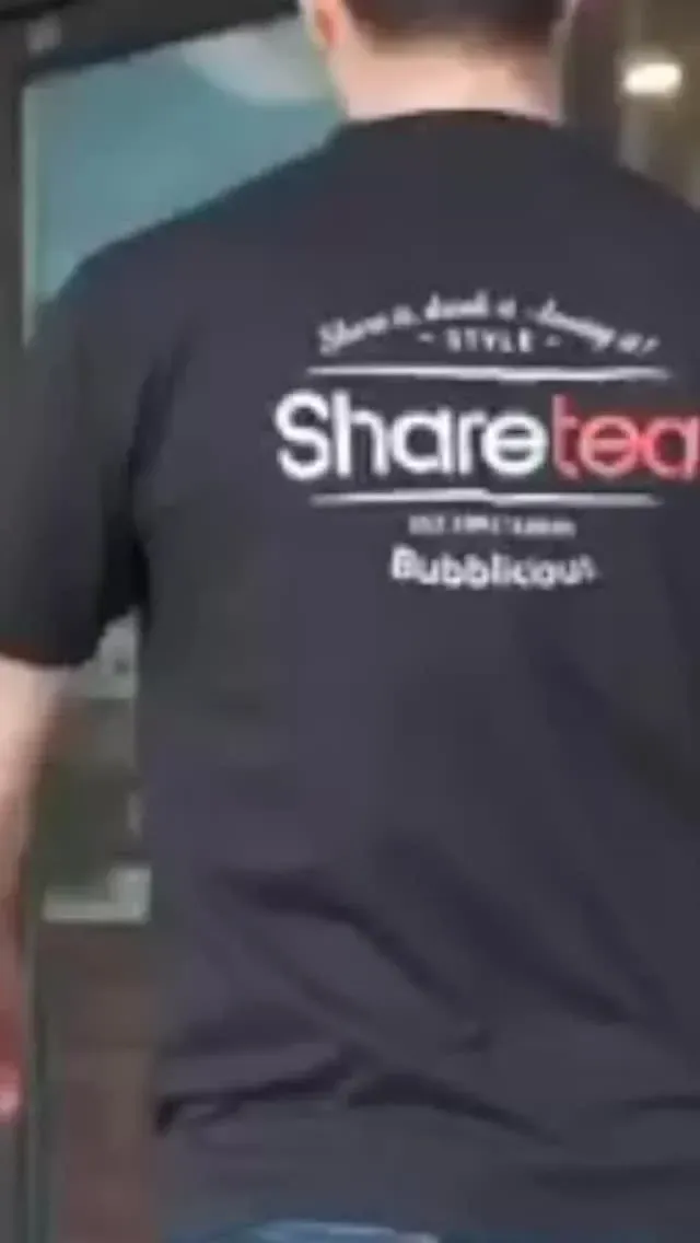 Person in a black T-shirt with the “Sharetea” logo on the back, standing indoors.