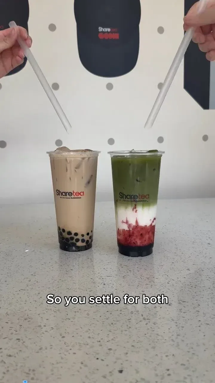 Two bubble tea drinks on a countertop, one beige and one layered green, white, and red, with hands holding chopsticks above them