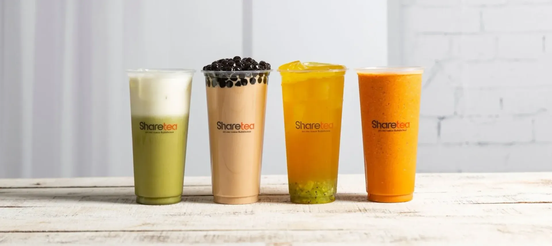 Four colorful beverage cups lined up on a light wooden surface against a white background