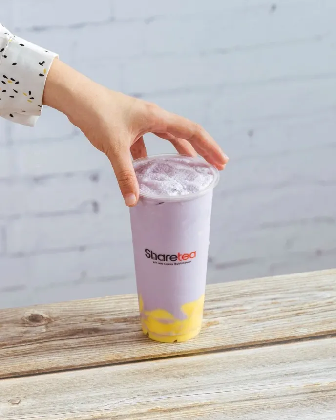 Hand placing a clear lid on a lavender plastic cup with yellow liquid on a wooden table