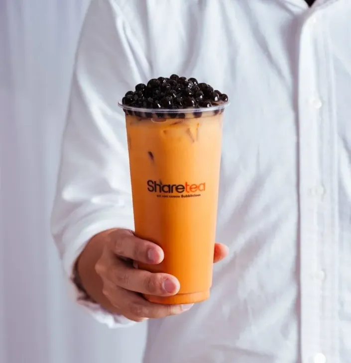 Hand holding an orange bubble tea topped with black tapioca pearls in a clear cup