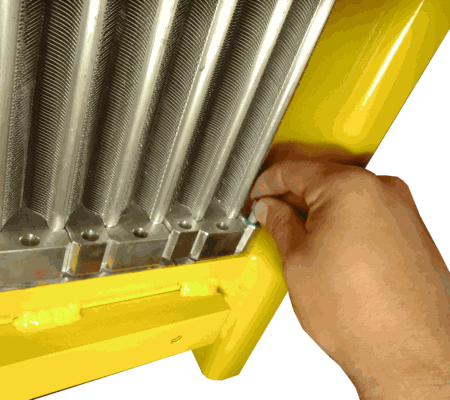 A hand aligns a metal bolt into a hole on the silver heat exchanger frame attached to a yellow industrial component.