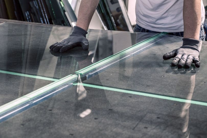 A man is cutting a piece of glass on a table.