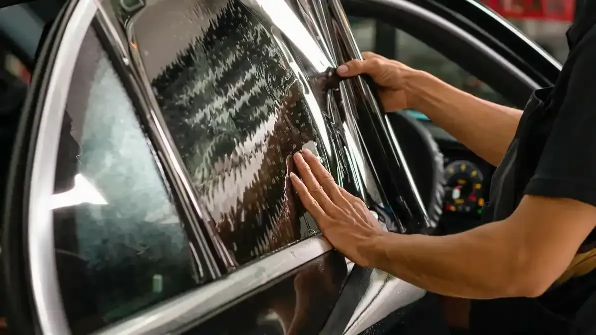 A person is applying tinted window film to a car window.