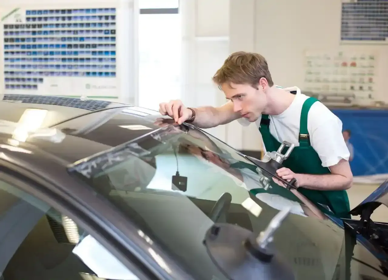A man in green overalls is working on a car windshield