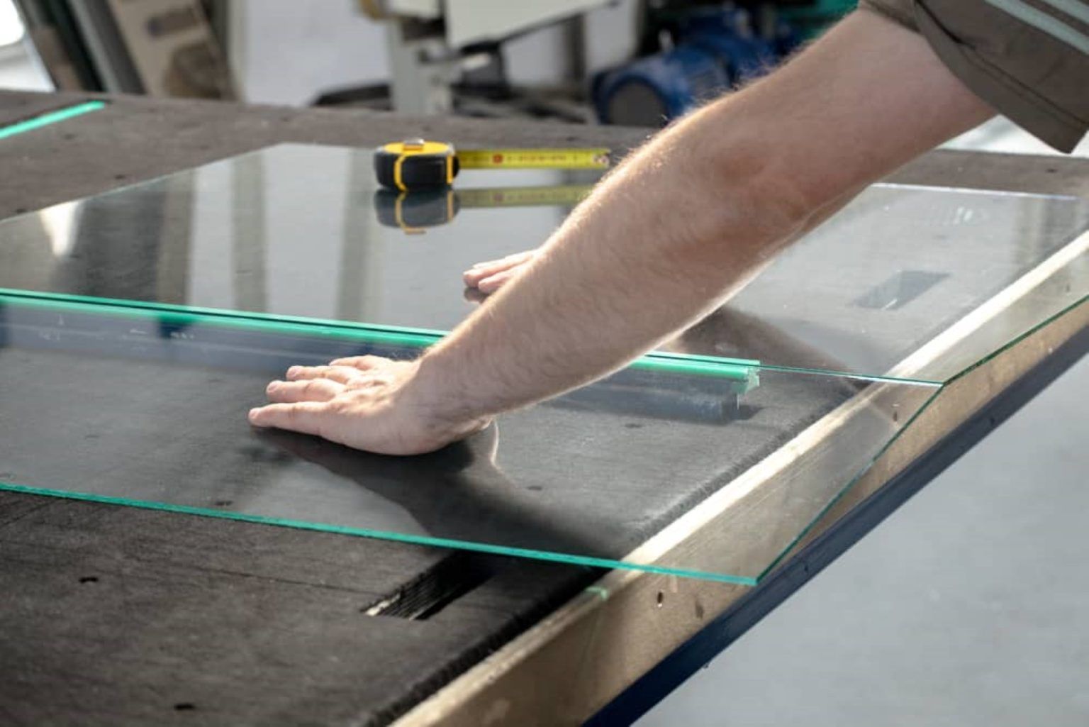 Person measuring and working with a glass panel on a workbench, with a tape measure present.