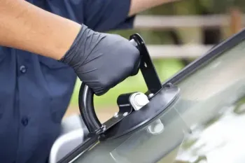 A man is using a suction cup to remove a windshield from a car.