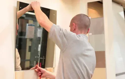 A man is hanging a mirror on a wall.