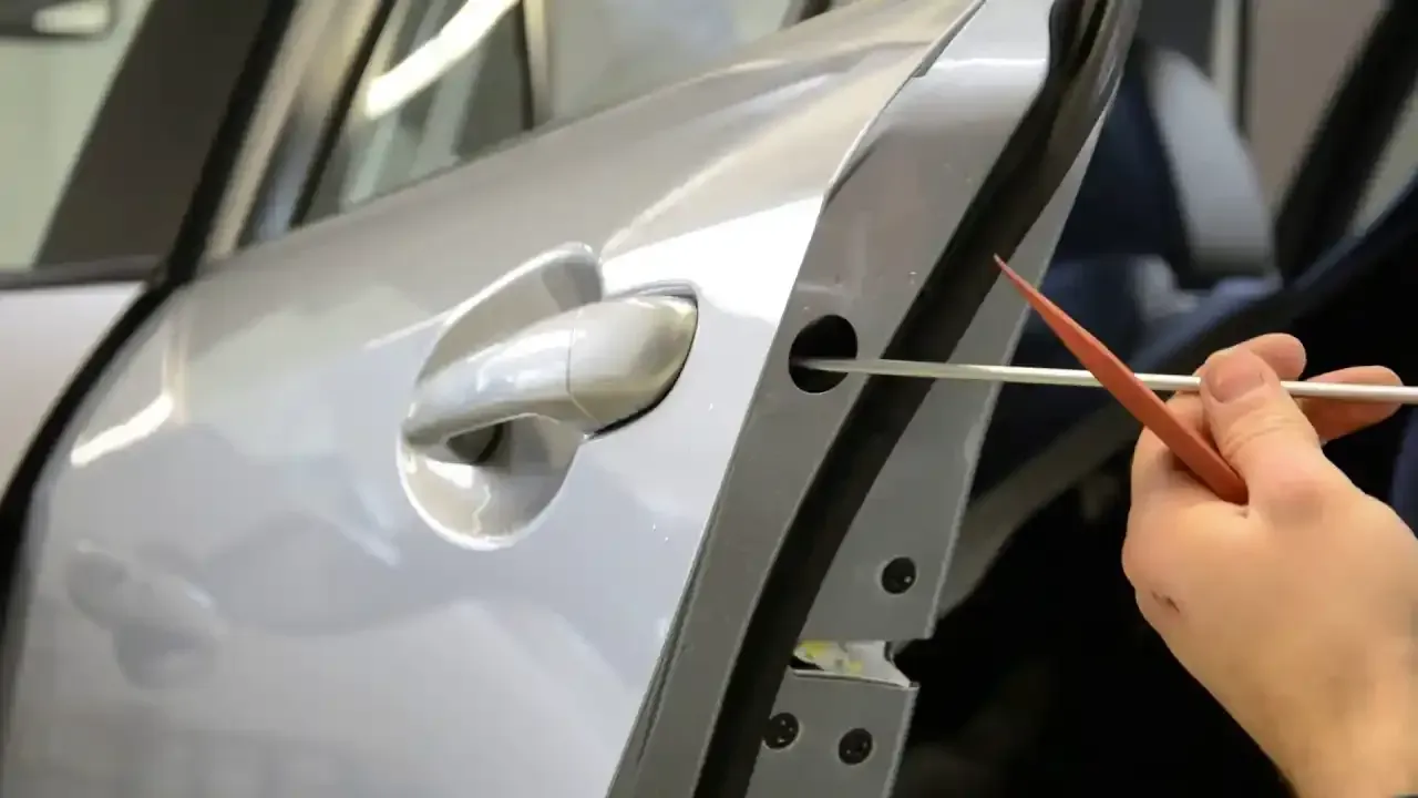 A person is opening a car door with a screwdriver.