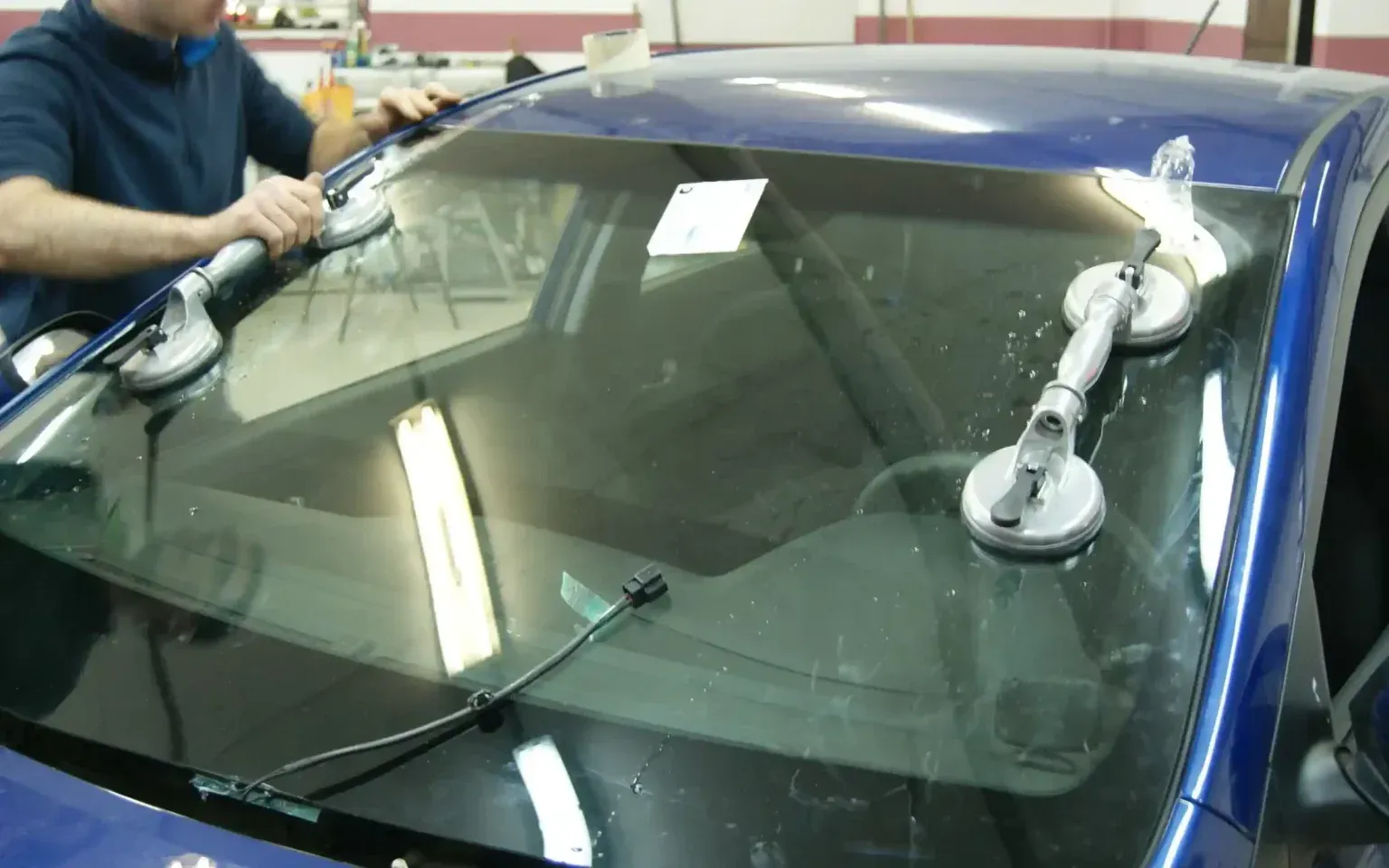A man is installing a windshield on a blue car.