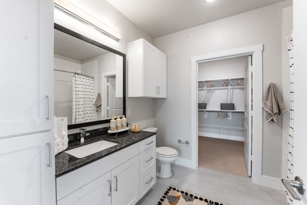 A bathroom with a sink, toilet, mirror and walk in closet at The Bennett, which offers apartments for rent in South Austin, TX.