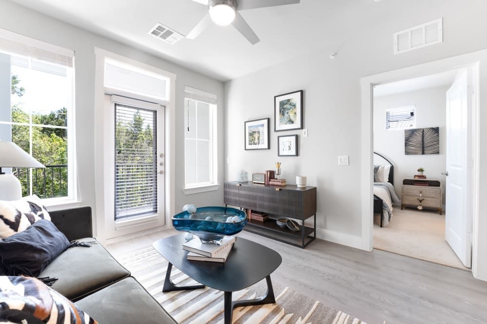 A living room with a couch, coffee table, exit to balcony and ceiling fan at The Bennett, which offers apartments for rent in South Austin, TX.