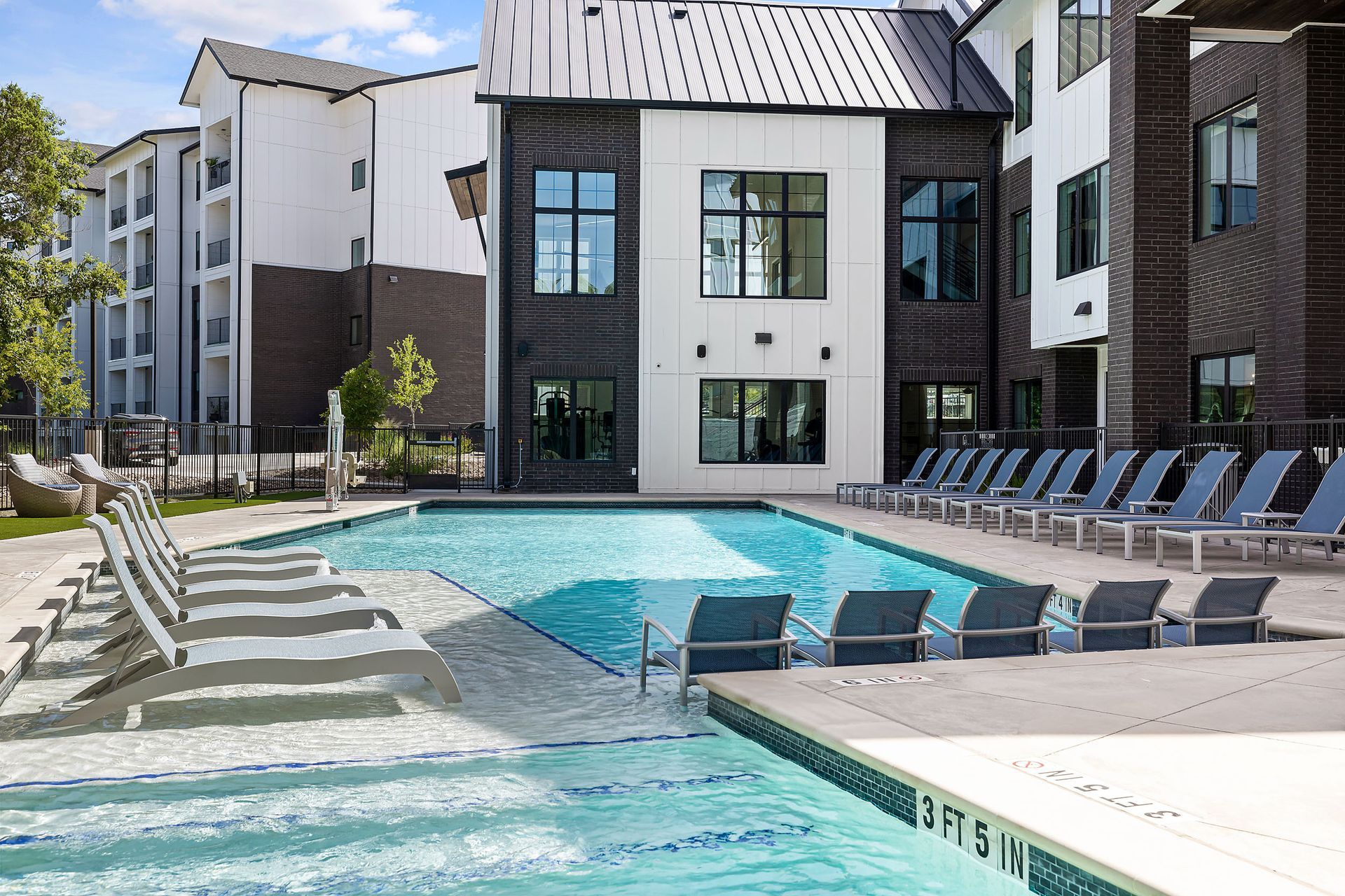 A large swimming pool surrounded by chairs in front of a building at The Bennett, which offers apartments for rent in South Austin, TX.