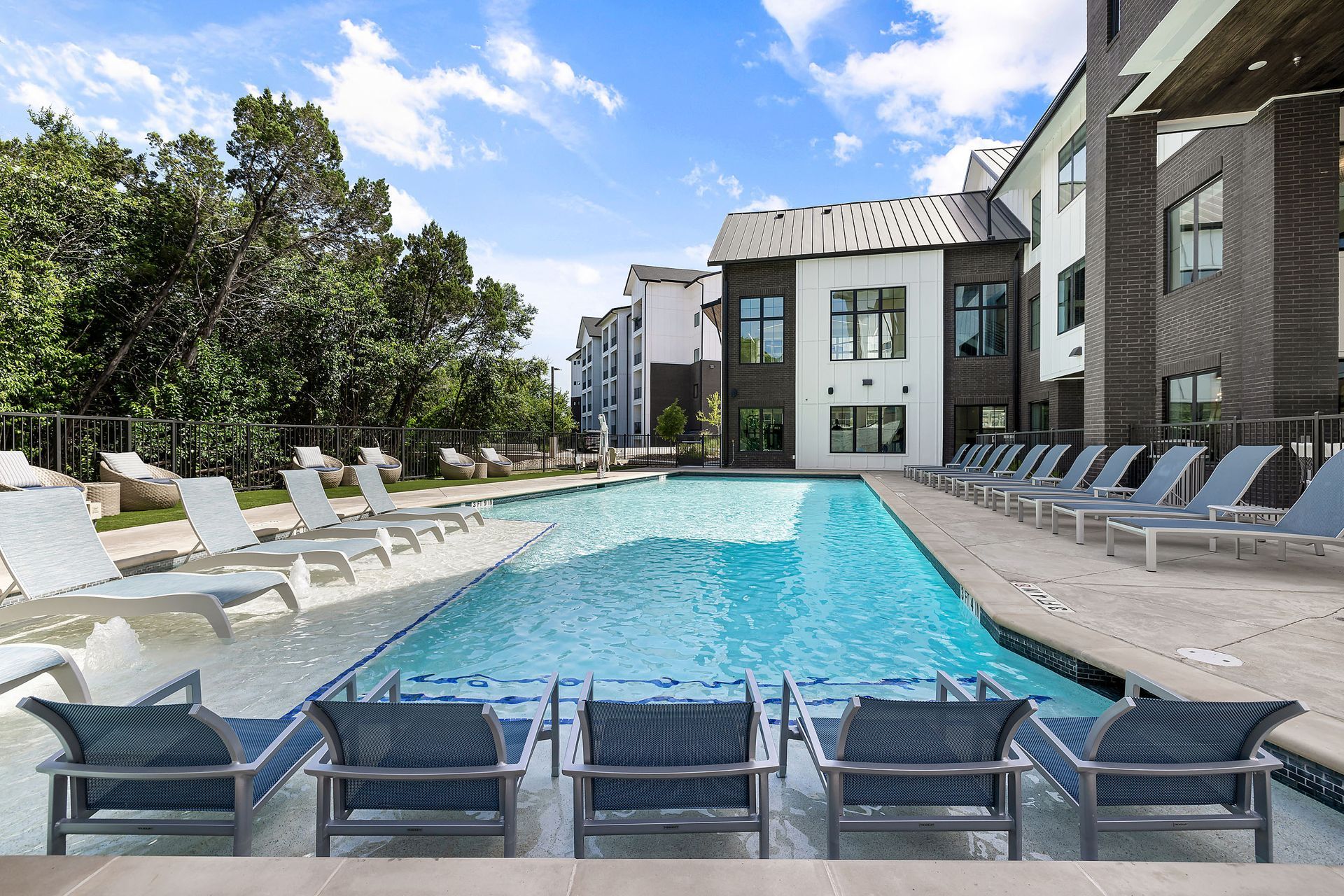 A large swimming pool surrounded by chairs and a building at The Bennett, which offers pet-friendly apartments for rent in South Austin, TX.