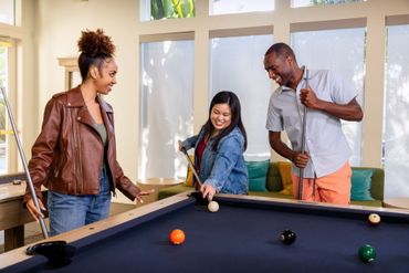 Three people playing pool in a room, smiling around a billiards table Sequoia West Coast Multifamily Property Management.