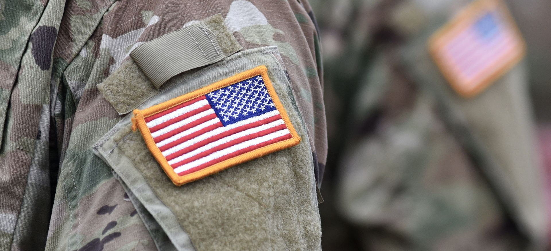 Veterans in dress uniforms at a memorial ceremony, with an American flag in the background