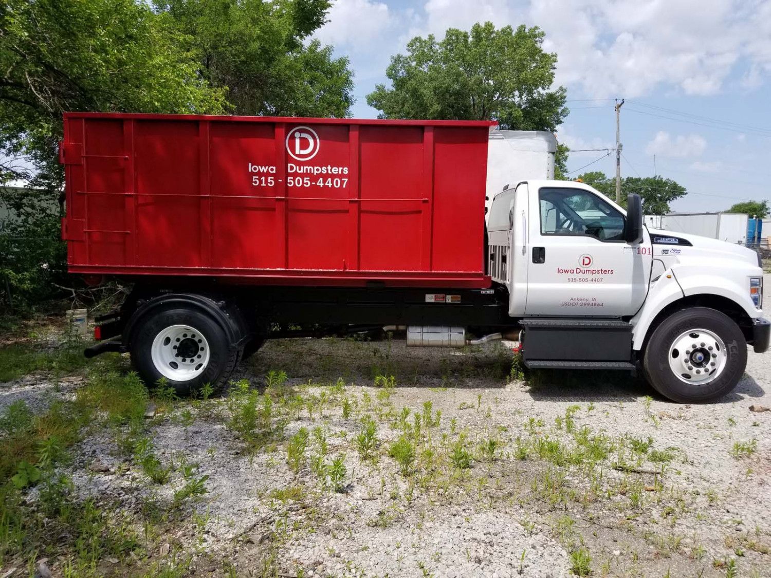Red dumpster truck parked outdoors with logo and contact info.