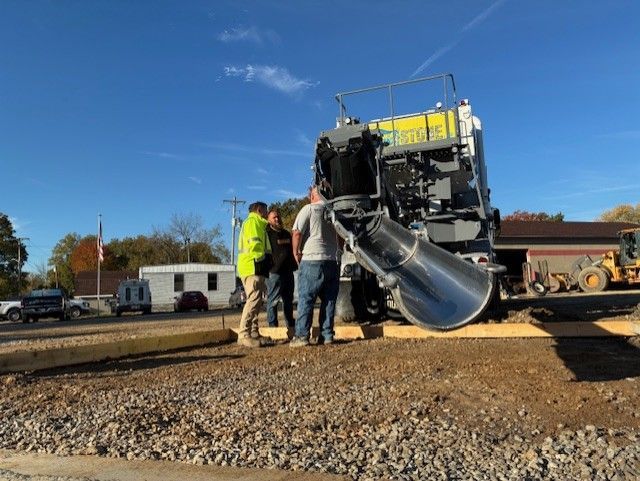 Workers loading asphalt into a paving machine on a road construction site