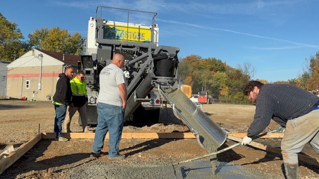 Liquid Stone workers operate paving machinery at an outdoor construction site on a sunny day.