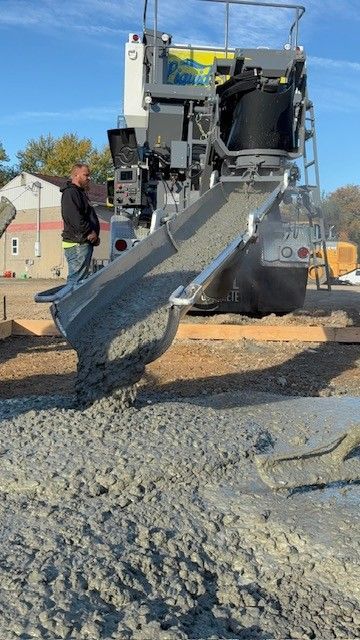 On-site concrete mixing pouring wet concrete onto a road surface, with a worker standing nearby.