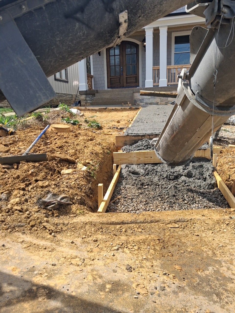Construction site with foundation trenches, gravel, and pipes near a house exterior