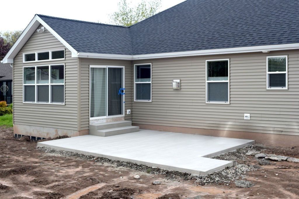 A new house with beige siding and a dark roof features a small concrete patio.