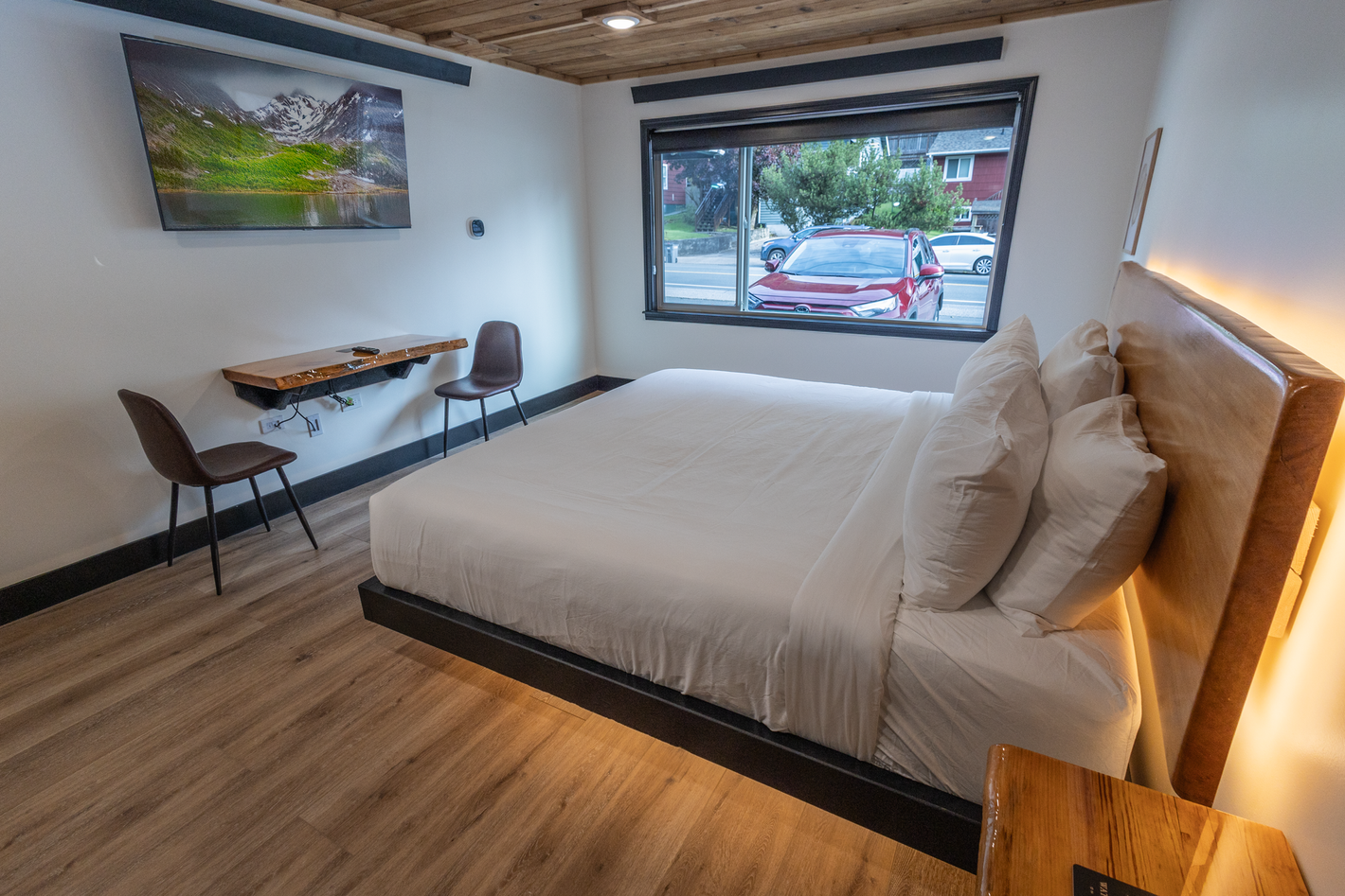 A hotel room with a bed , desk , chairs and a large window.