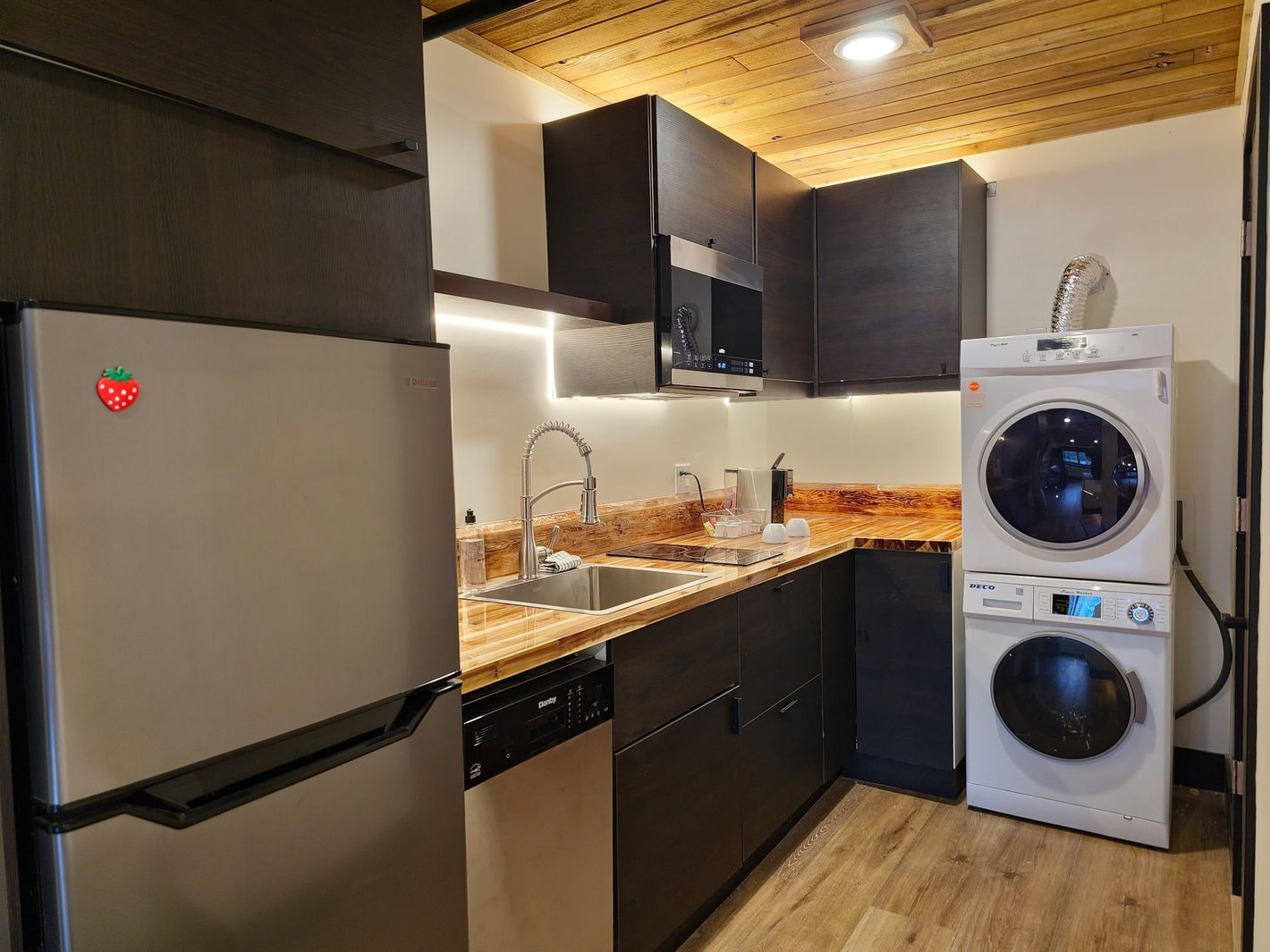 A kitchen with a refrigerator , sink , washer and dryer stacked on top of each other.