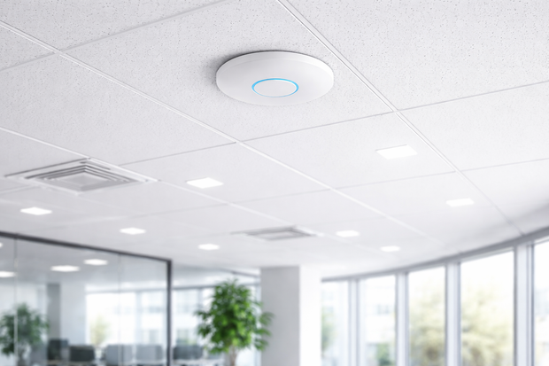 Modern office ceiling with recessed lights, air vents, and a circular smoke detector over glass walls and plants
