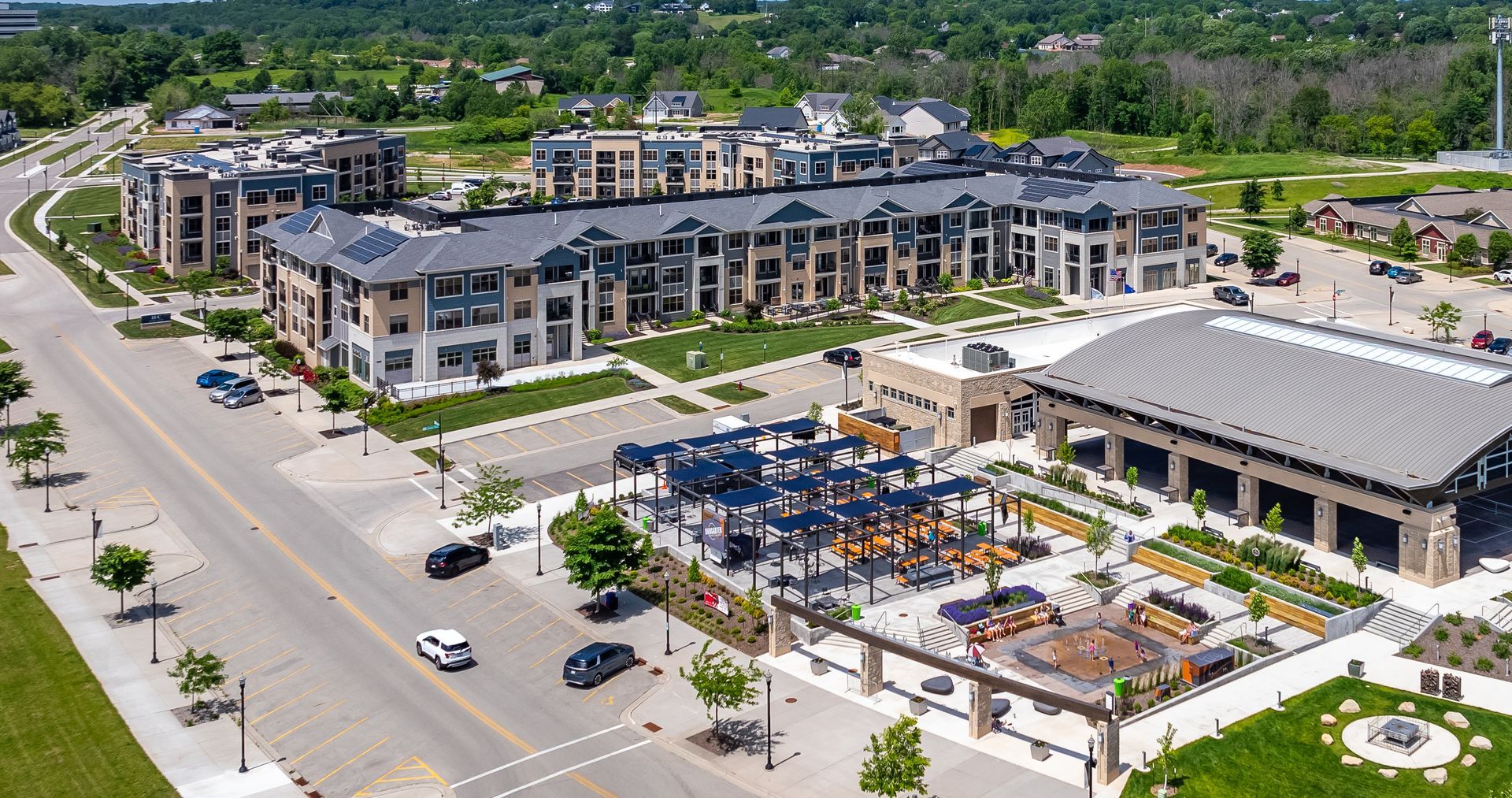 Aerial view of a modern apartment complex with a pool, parking lot, and surrounding trees