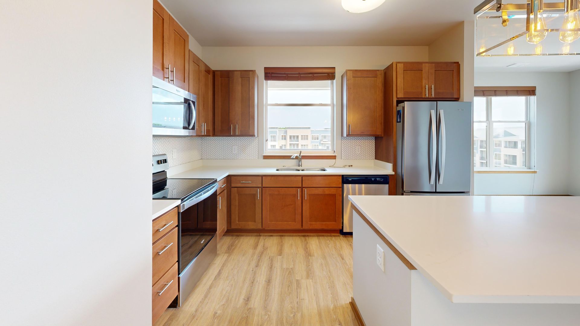 Bright kitchen with wooden cabinets, stainless steel fridge, and large white island counter.