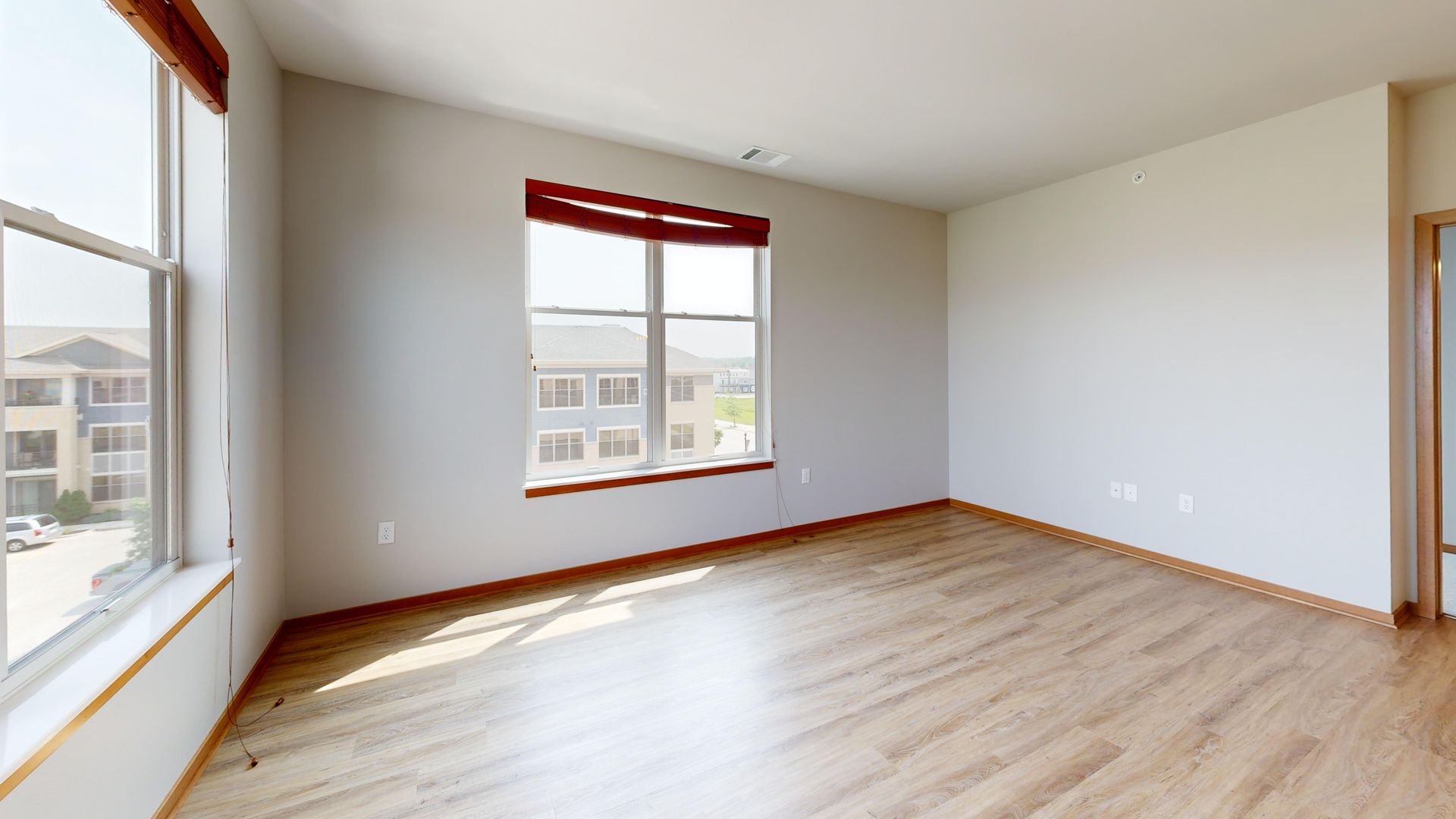 Empty bright room with light wood floors, white walls, and two windows with red blinds