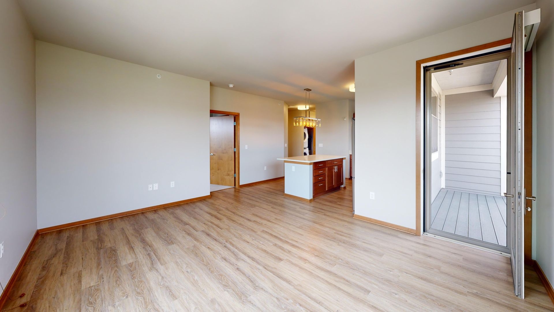 Empty modern living room with light wood floors, white walls, and open doorway to a balcony