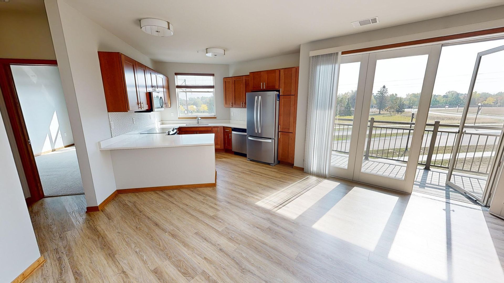 Bright modern kitchen and dining area with wood floors, white island, stainless fridge, and sliding glass doors to a deck.