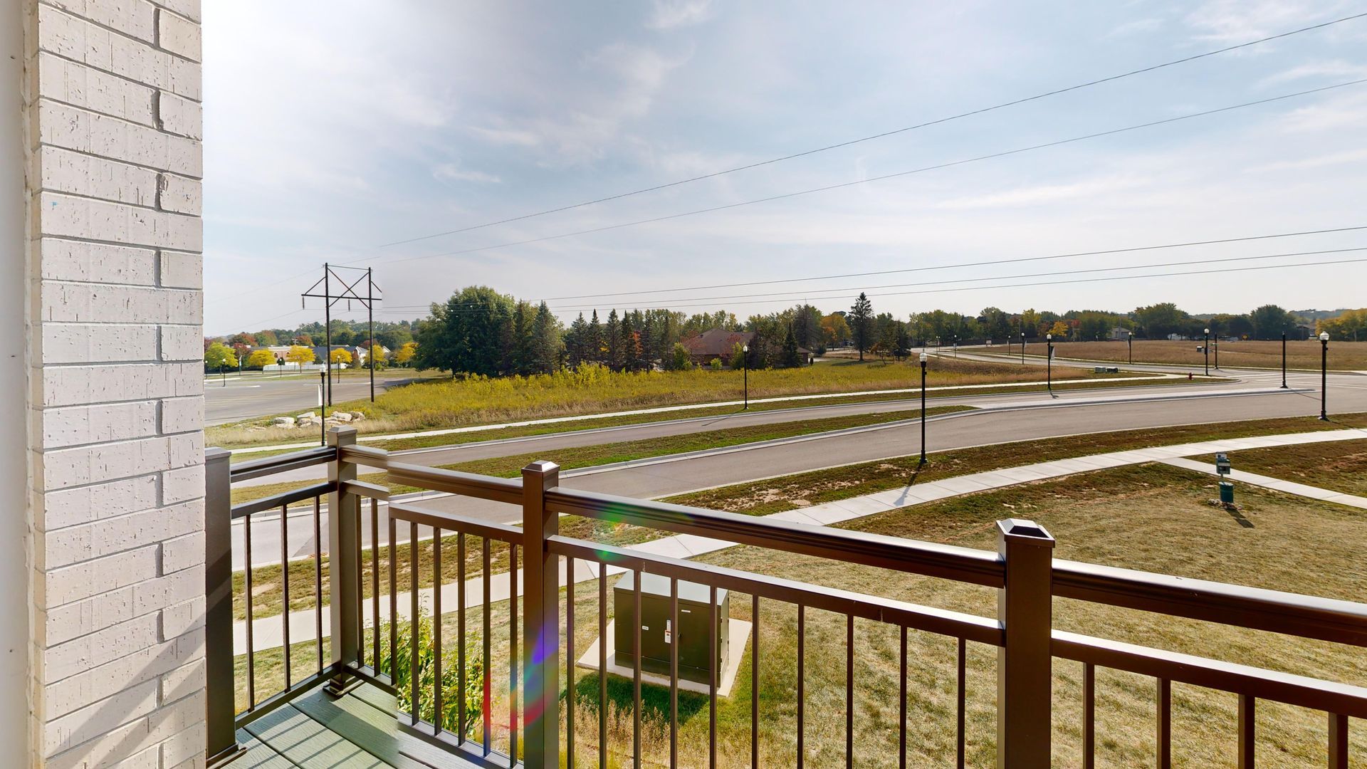 Balcony overlooking a landscaped neighborhood with roads, lawns, and a cloudy sky
