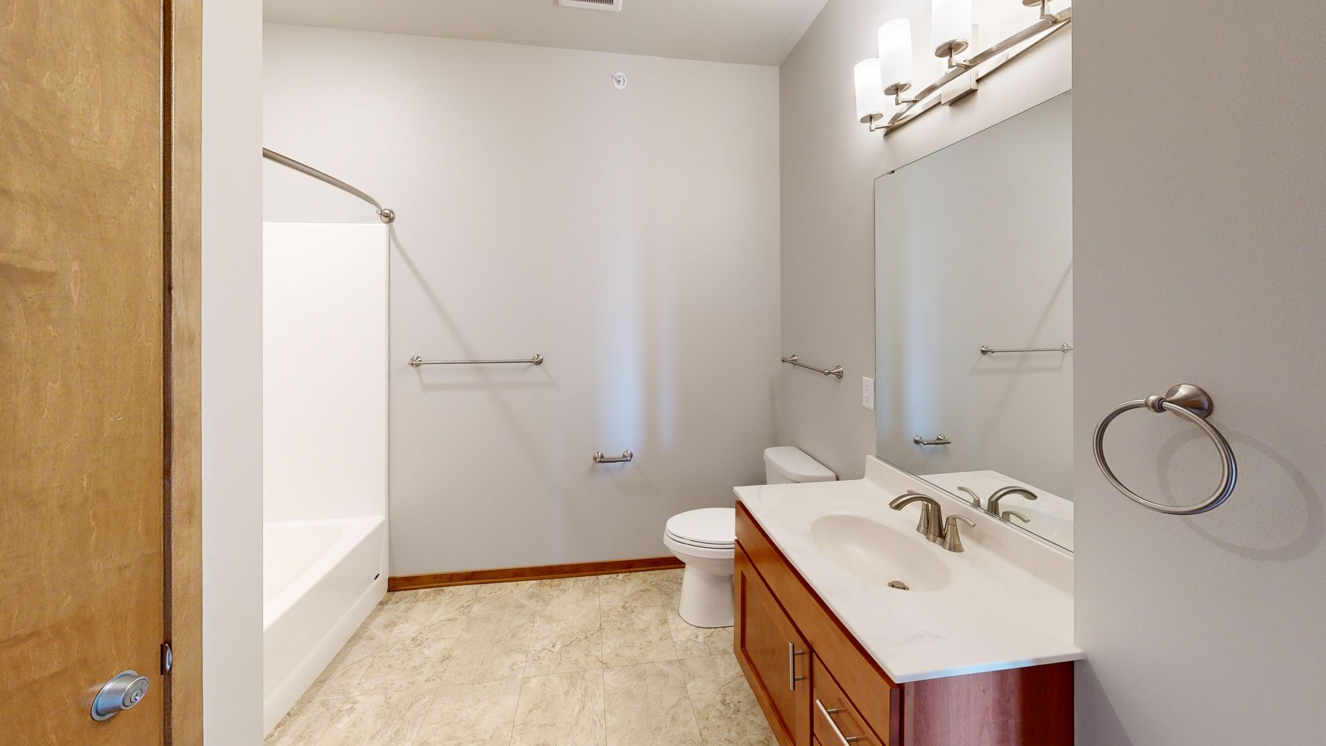 Bathroom with white walls, shower tub, toilet, and wood vanity with mirror and lights