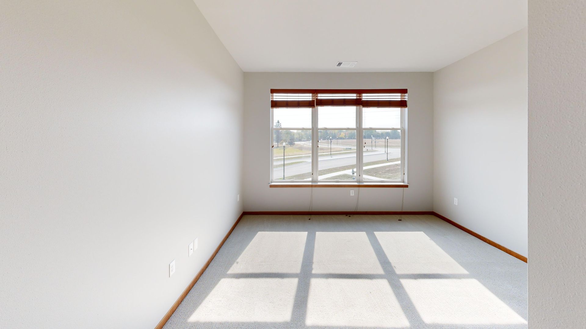 Empty white bedroom with a window and sunlight casting shadows on the floor