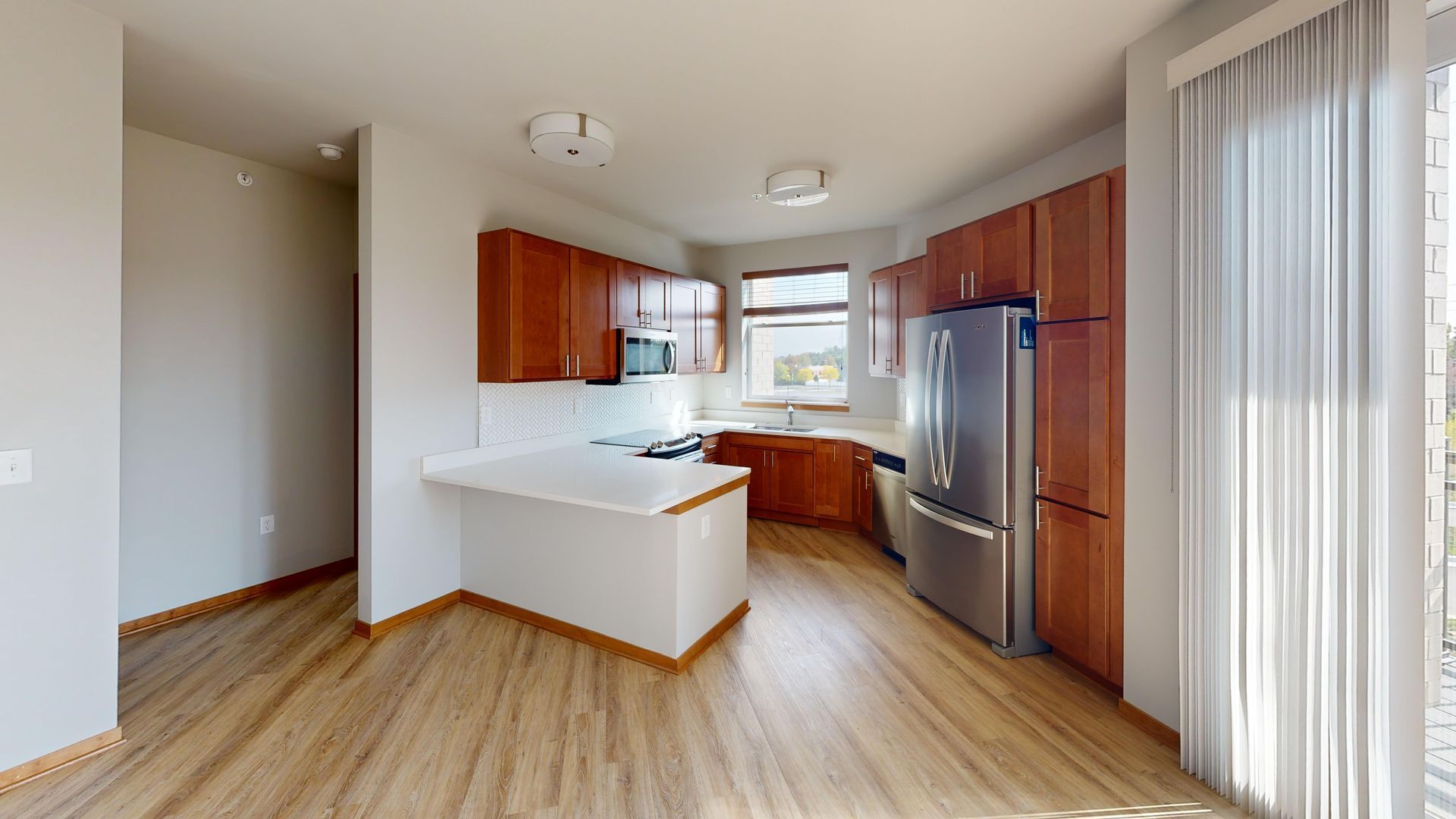 Modern kitchen with wood cabinets, white island, stainless steel appliances, and large window blinds