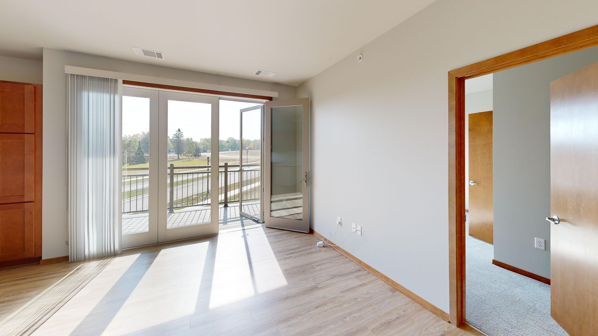 Bright empty room with sliding glass doors, balcony view, and a doorway to a carpeted room