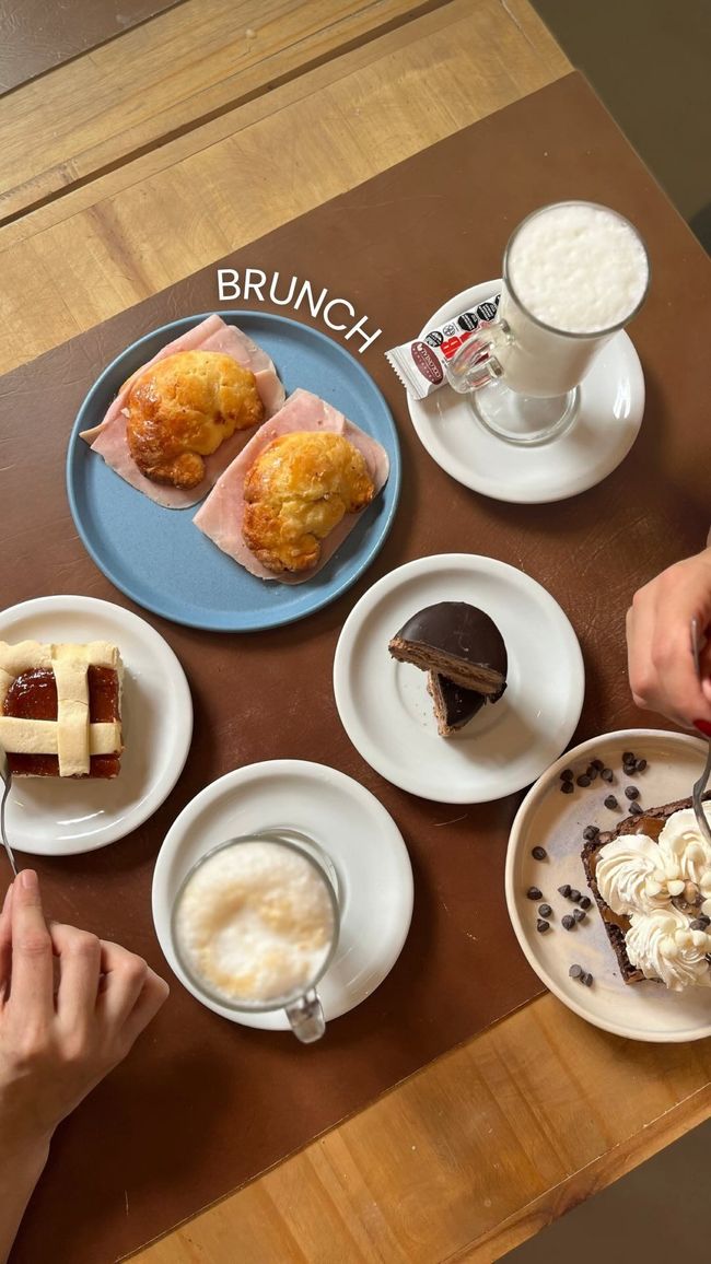 Vista aérea de una mesa de brunch con pasteles, bebidas de café y platos sobre una superficie de madera.