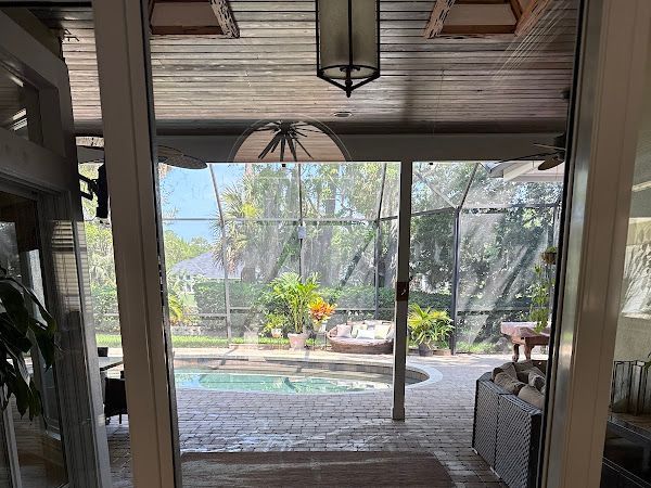 Patio view through screened doors to a backyard pool, palm trees, and outdoor seating.