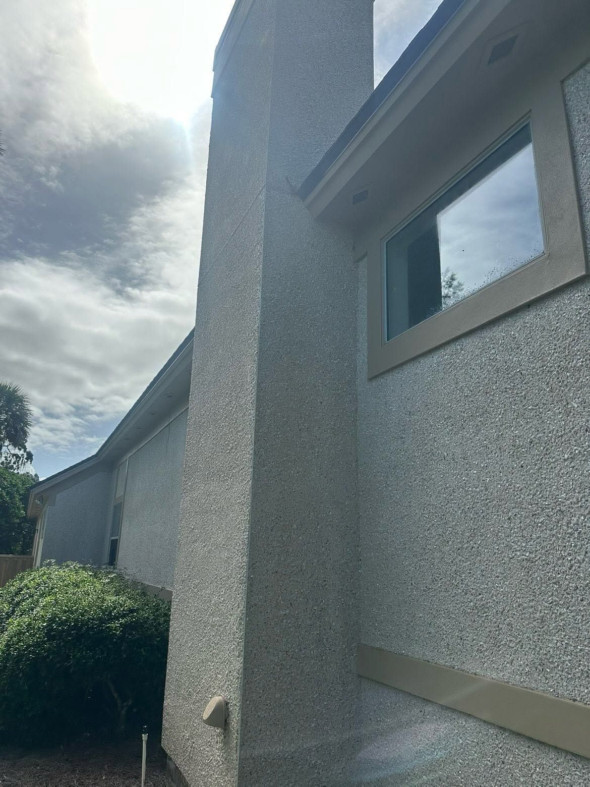 Exterior of a beige stucco house with a window and cloudy sky overhead