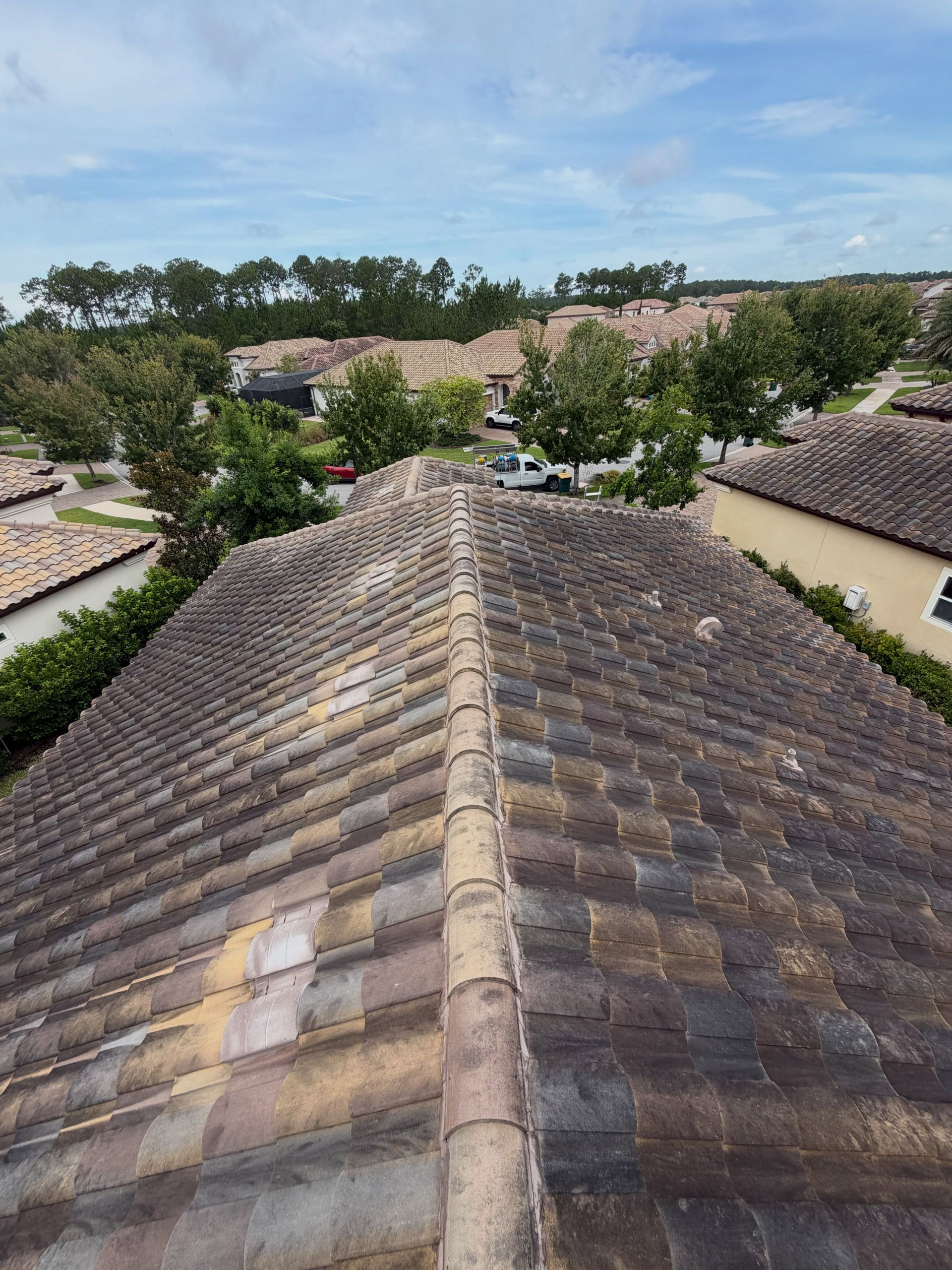 Roof ridge view over tiled rooftops and trees under a partly cloudy sky