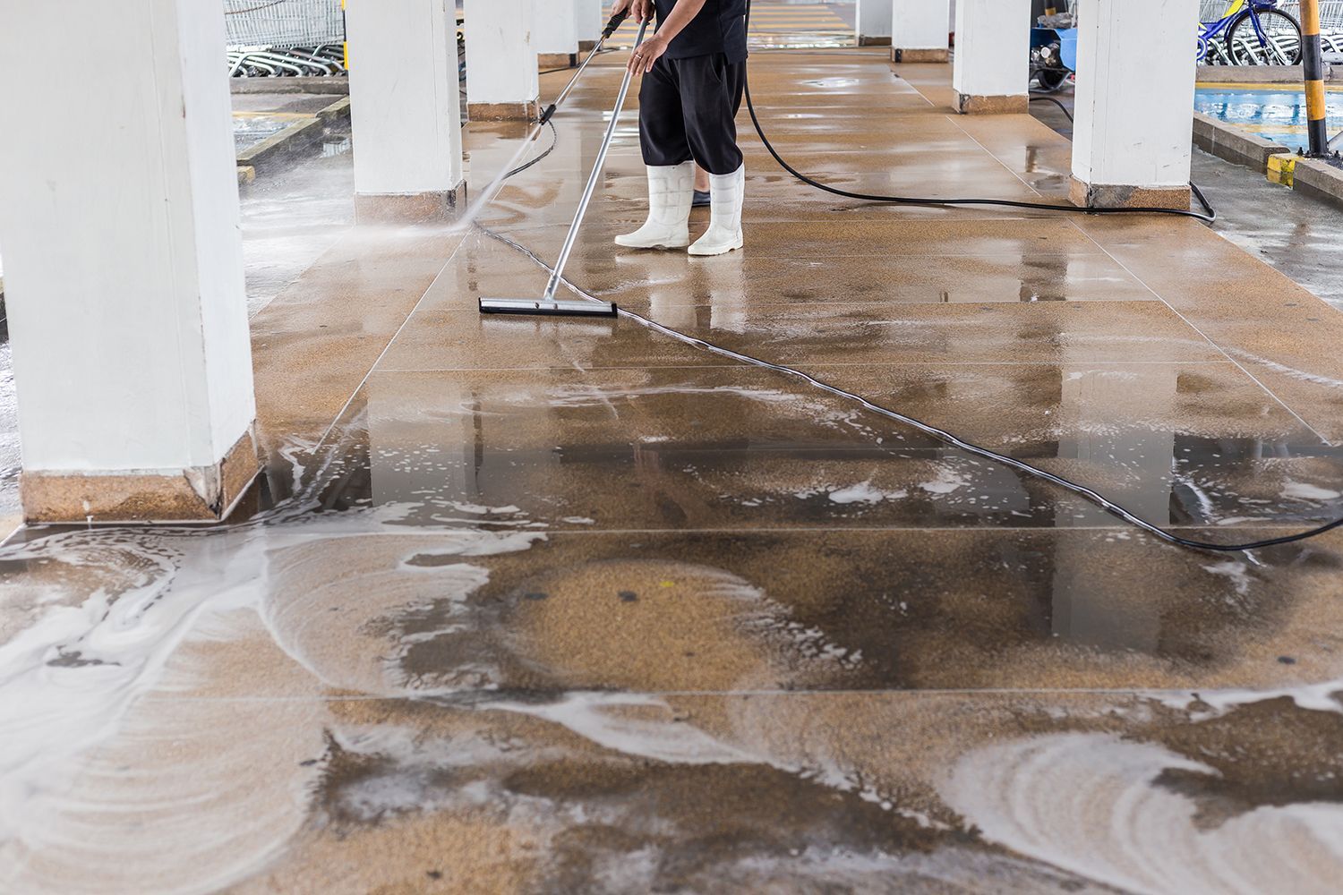 Person pressure-washing a wet concrete floor in a covered industrial space Person pressure-washing a wet concrete floor in a covered industrial space