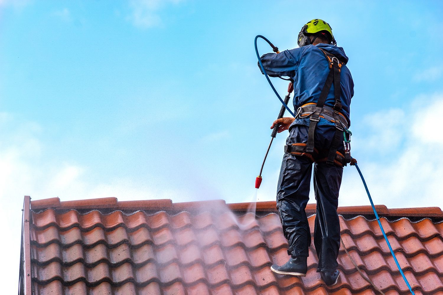 Worker on a tiled roof spraying water with a hose, wearing safety gear and harness. Worker on a tiled roof spraying water with a hose, wearing safety gear and harness.