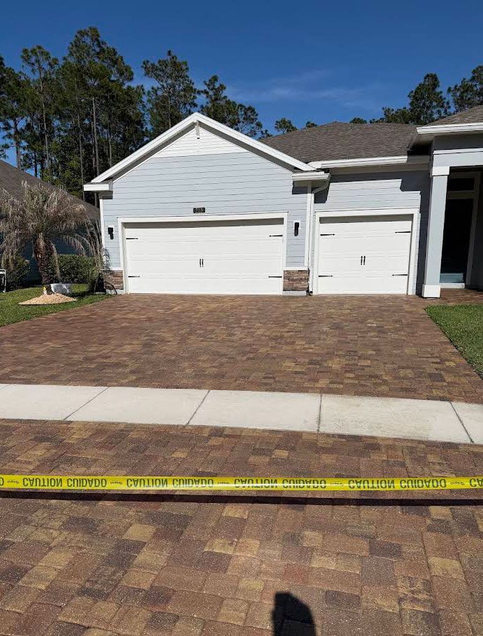 Suburban house with two white garage doors and a brick driveway, marked by yellow caution tape in front